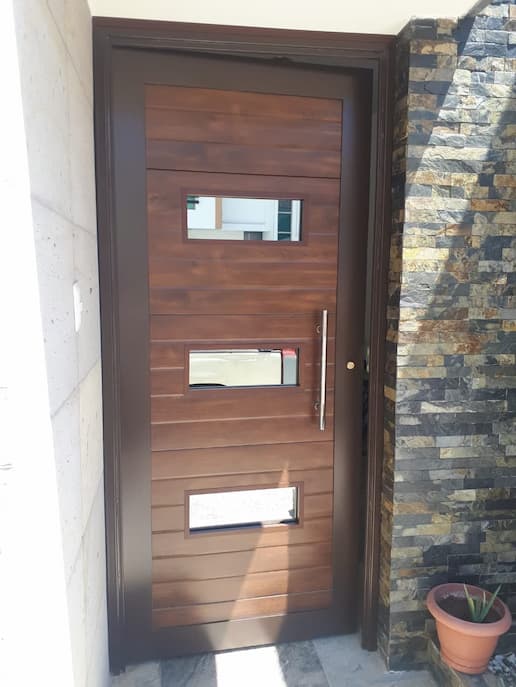 Puerta para casa de material de porton imitación madera oscuro con tres ventanas.